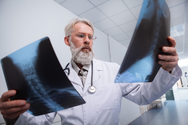 Radiologista masculino idoso experiente olhando para exames de raio-x da coluna vertebral de um paciente