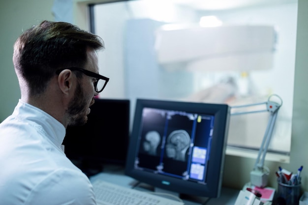 Radiologista masculino revisando os resultados da ressonância magnética cerebral no computador na sala de controle na clínica