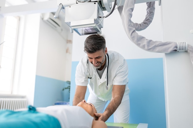 Radiologistas multiétnicos com jovem paciente do sexo feminino na sala de raio-x Radiologista configurando a máquina para fazer o raio-x do paciente do sexo feminino