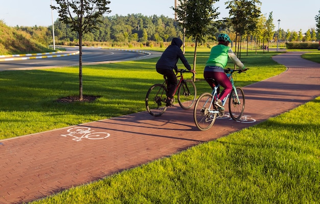 Radweg im öffentlichen Park der Stadt mit zwei Radfahrern, die am frühen Morgen fahren. Aktiver Lebensstil.