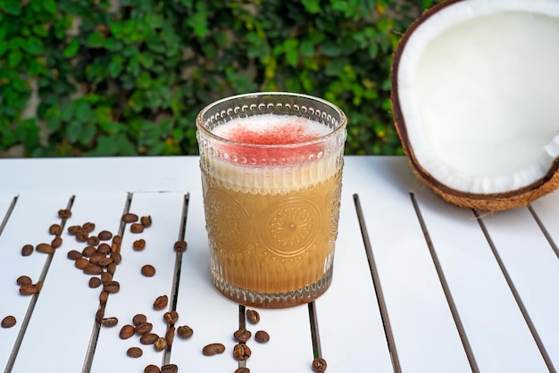 Raf café coco com coco fresco e grãos de café na mesa de madeira branca contra folhas verdes wi