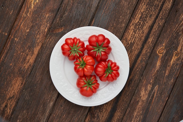 Raf de tomates vermelhos frescos na chapa branca no fundo de madeira Conceito de comida