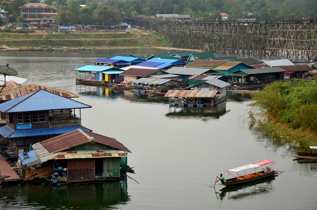 Raft House y gente remando en bote de madera en el río Samprasob cerca del puente de madera Saphan Mon en Sangkhlaburi el 4 de diciembre de 2015 en Kanchanaburi Tailandia