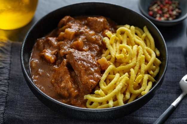 Ragu de carne com macarrão servido em uma tigela em fundo escuro. Fechar-se.