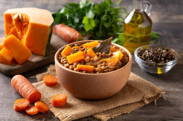 Ragu de guisado de lentilha com abóbora e cenoura em tigela na mesa de madeira