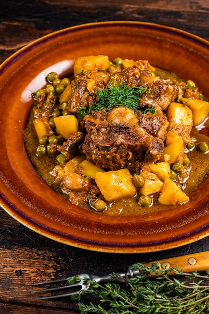 Foto ragú de rabo de toro de cordero con verduras en un plato rústico. fondo de madera oscura. vista superior.