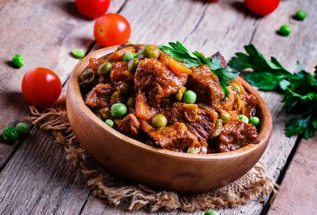 Ragú con zanahorias de ternera, guisantes y tomates, fondo de madera antiguo, enfoque selectivo