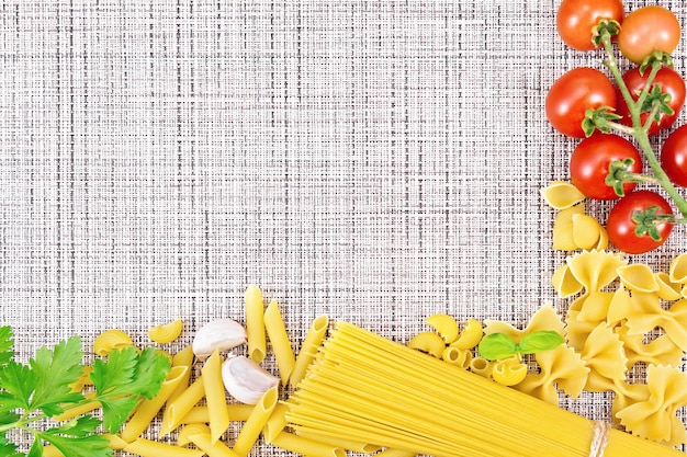 Rahmen aus verschiedenen Nudeln, Tomaten, Knoblauch und Petersilie auf einem Hintergrund aus Weidenstoff
