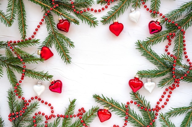 Rahmen aus Weihnachtsbaumzweigen und Glasdekorationen in Form von Herzen.