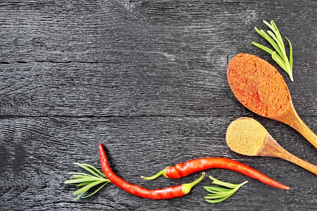 Rahmen aus Zweigen mit frischem Rosmarin, Schoten mit rotem Paprika und zwei Löffeln mit gemahlenem Pfeffer