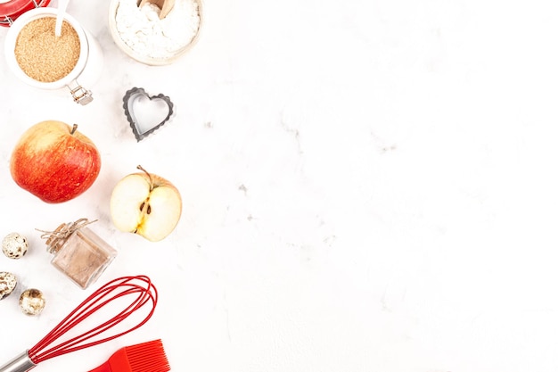 Rahmen mit Backzutaten zum Valentinstag, ein kulinarischer Hintergrund mit Gebäck - Schneebesen zum Schlagen, Keksformen, Äpfel, Zucker, Mehl. Weißer Hintergrund, Platz zum Kopieren der Draufsicht