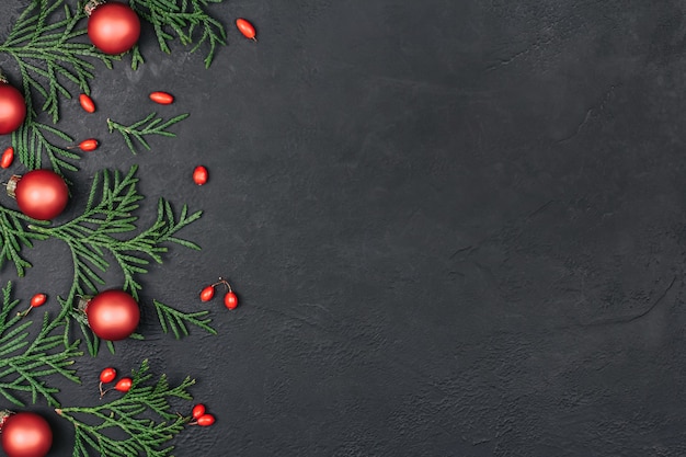 Foto rahmen von grünen zweigen und roten weihnachtskugeln auf einem schwarzen