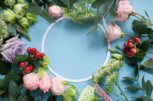 Rahmen von lila und rosa Rosen, weißem Lisianthus und verschiedenen Blumen auf blauem Hintergrund.