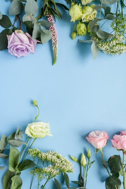 Rahmen von lila und rosa Rosen, weißem Lisianthus und verschiedenen Blumen auf blauem Hintergrund.