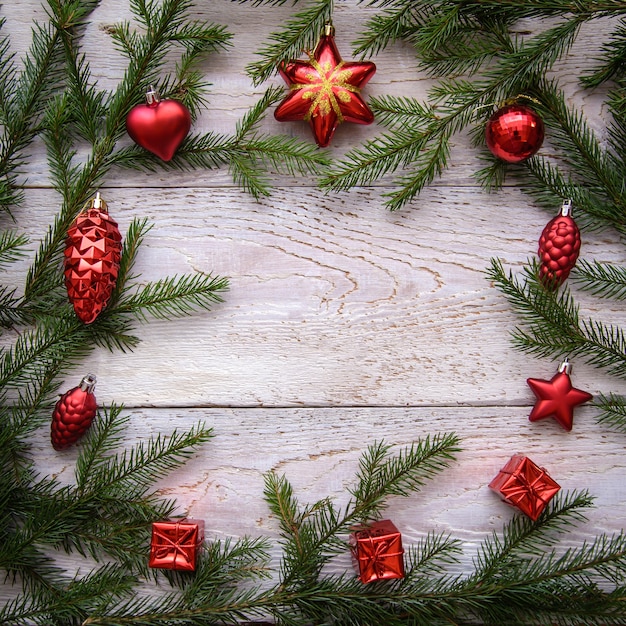 Rahmen von Weihnachtsbaumzweigen und roten Verzierungen auf einem hellen hölzernen Hintergrund