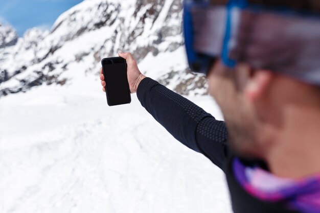 Rahmenbild eines Snowboarders in der Wintersportkleidung, die Selfie-Foto mit seinem Handy an den schneebedeckten Bergen macht