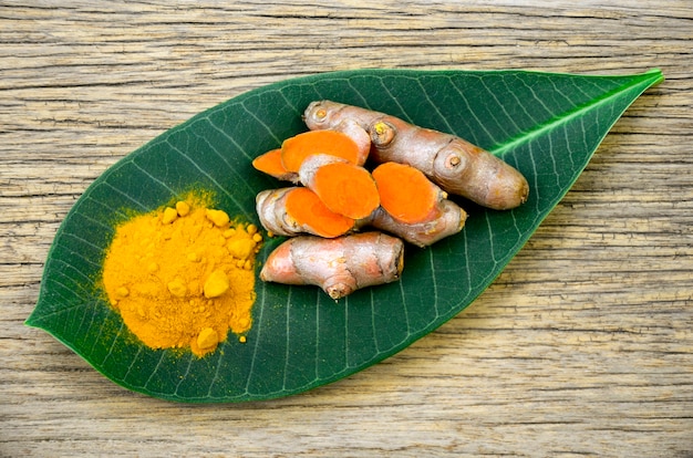 Foto raíces de cúrcuma y poder de la cúrcuma en el fondo verde de la hoja y de madera.