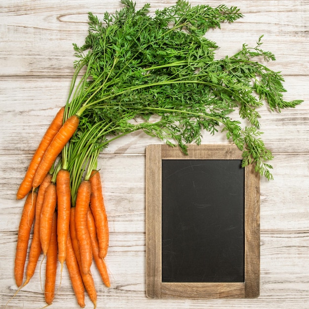 Raíces de zanahorias frescas hojas verdes y pizarra Alimentos orgánicos