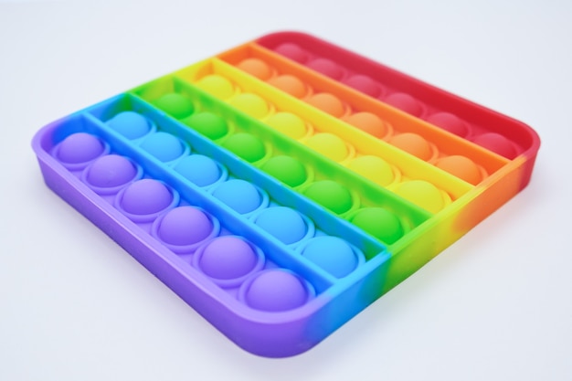 Rainbow Square Fidget Toys Pop-it en el fondo claro. Empuje Pop Bubble. Popular juguete relajante de silicona de forma cuadrada para aliviar el estrés. Vista desde un ángulo en perspectiva.