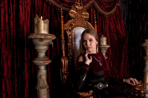 Rainha medieval em trajes históricos no trono dourado do castelo. retrato de jovem em um vestido de estilo antigo em um trono antigo na sala de recepção da fortaleza. conceito de eventos temáticos de fantasias