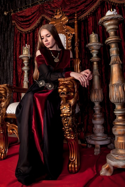 Rainha medieval em trajes históricos no trono dourado do castelo. Retrato de jovem em um vestido de estilo antigo em um trono antigo na sala de recepção da fortaleza. Conceito de eventos temáticos de fantasias