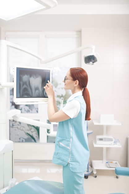 Raio X do paciente. Dentista profissional ruivo com rabo de cavalo estudando radiografia de paciente