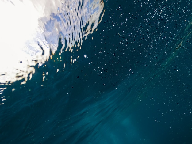 Raios de luz solar brilhando de cima vindo através da água azul profunda causando uma cortina de reflexos. As ondas subaquáticas do oceano oscilam e fluem. Raios de luz na cena criam um lindo véu