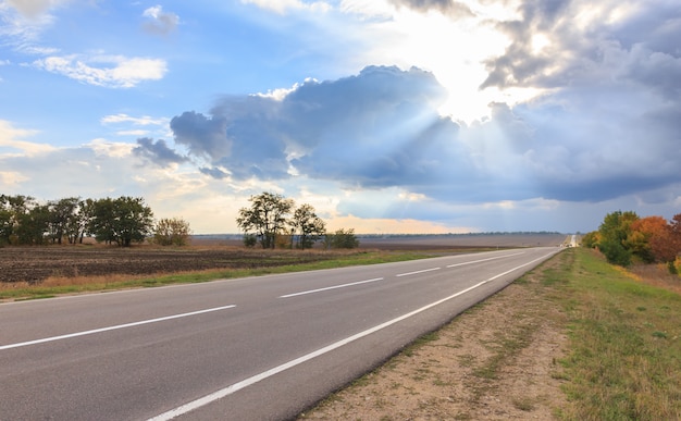 Raios de sol estão rompendo as nuvens e a estrada vazia