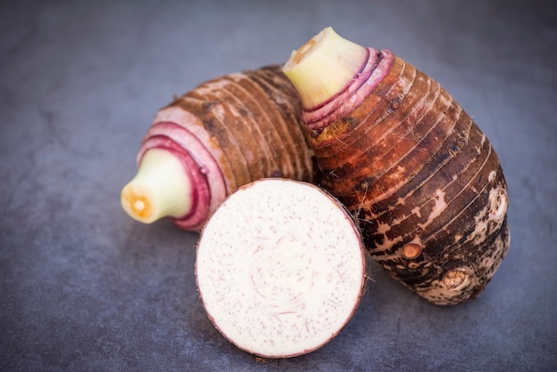 Raiz de taro com meia fatia em fundo escuro, raiz de taro orgânica crua fresca pronta para cozinhar