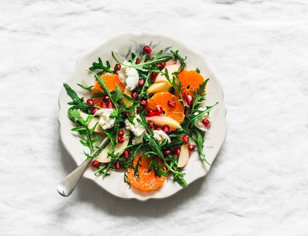 Raketensalat mit Mandarinen, Granatapfeln, Äpfeln und Mozzarella-Käse auf einem hellen Hintergrund