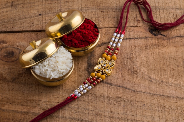 Un Rakhi con granos de arroz y kumkum sobre fondo de madera. Un fondo festivo indio.