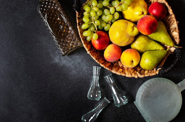 Rakia oder Rakija, der traditionelle Balkanfruchtbrand. Die Früchte davon produzieren Rakia. Früchte in einem Korb, Flaschen und Gläser für Alkohol. Draufsicht. Schwarzer Hintergrund. Platz für Text