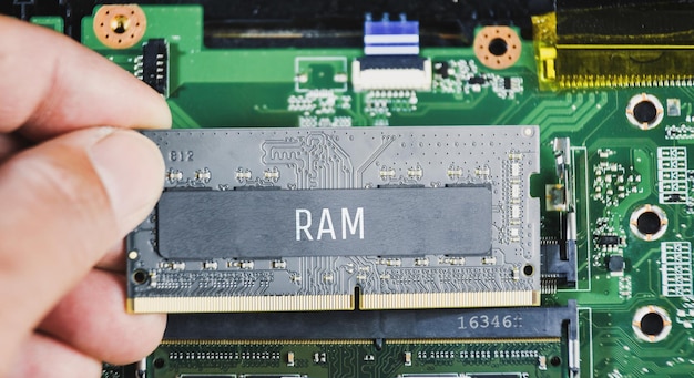 RAM (memoria de acceso aleatorio) DDR4 en la mano del técnico con un fondo de placa base de computadora portátil