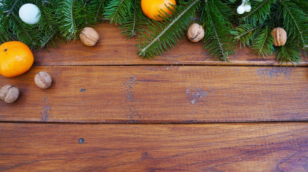 Rama de abeto y bolas de Navidad, nueces y mandarinas sobre fondo de madera