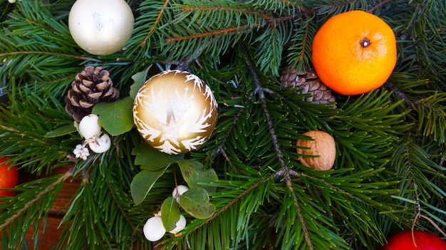 Rama de abeto y bolas de Navidad, nueces y mandarinas sobre fondo de madera