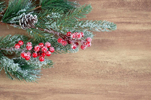 Rama de abeto de Navidad con bayas y conos rociados con nieve en un primer plano de fondo de madera con espacio de copia