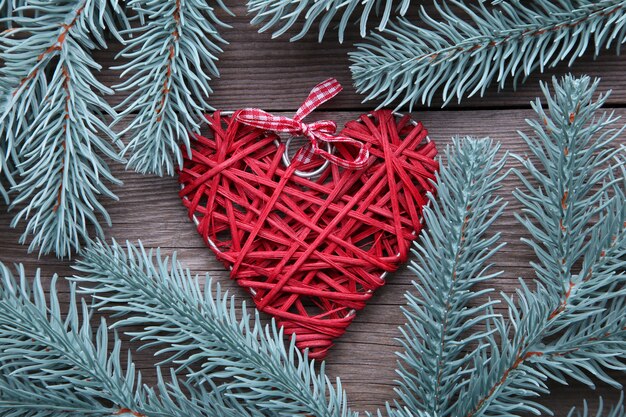 Rama de árbol de abeto con un corazón rojo sobre un fondo gris.