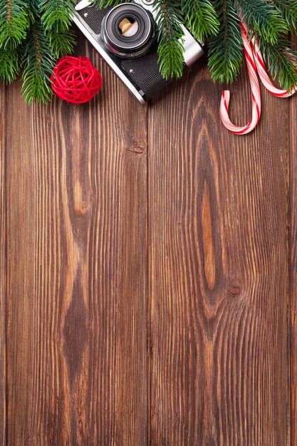 Rama de árbol de Navidad, cámara y bastón de caramelo en la mesa de madera. Vista superior con espacio de copia.