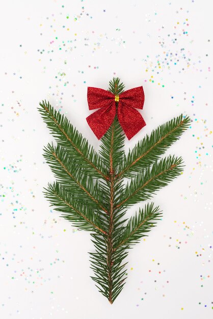 La rama de un árbol de Navidad está decorada con un lazo rojo sobre un blanco con purpurina.