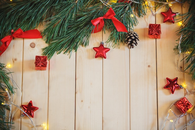 Rama de árbol de Navidad, lazo rojo, caja de regalo y guirnalda en mesa de madera clara.