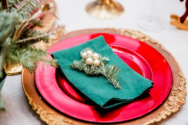 Una rama de árbol de Navidad con perlas se encuentra sobre una servilleta verde. La servilleta está en los platos festivos. Ajuste de la tabla de año nuevo. Foto