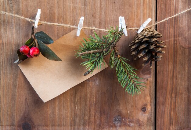 Rama de árbol de Navidad, piña y bayas de invierno en una cuerda con pinzas para la ropa. Deseando una feliz navidad