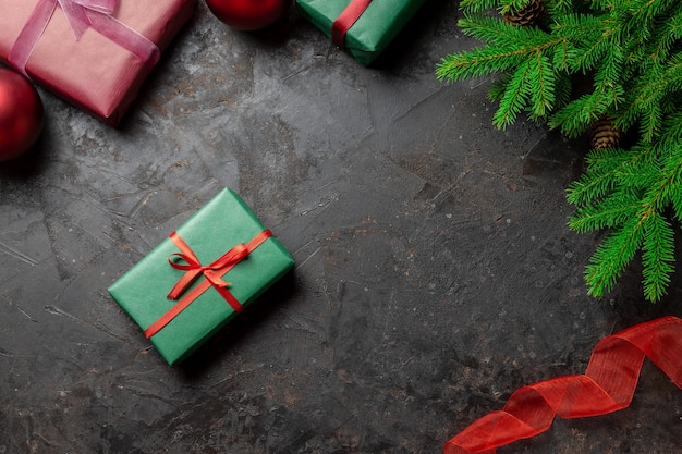 Rama de árbol de Navidad sobre fondo negro y caja de regalo con una cinta roja