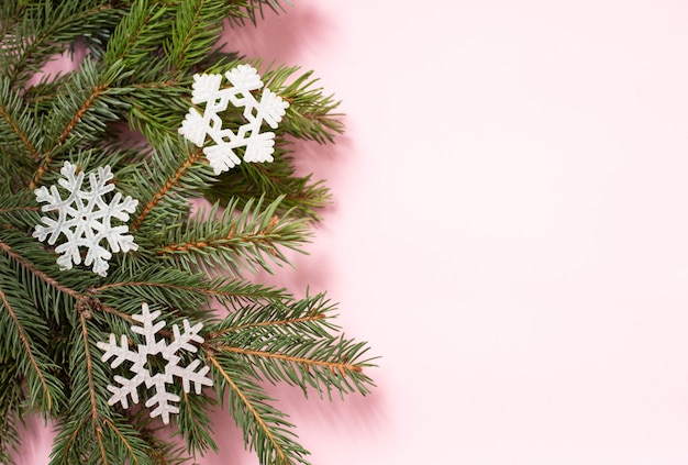 Rama de árbol de Navidad con tres copos de nieve blanca sobre fondo rosa con espacio de copia