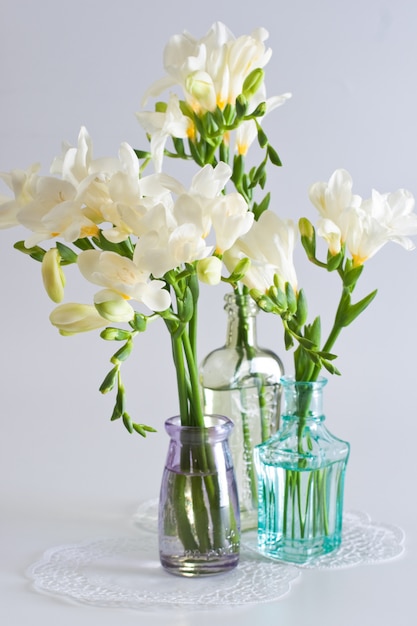 La rama de fresia blanca con flores y capullos en botellas decorativas.