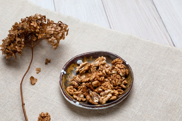 Rama de hortensia seca y tazón de cerámica con nueces en tela de lino grueso