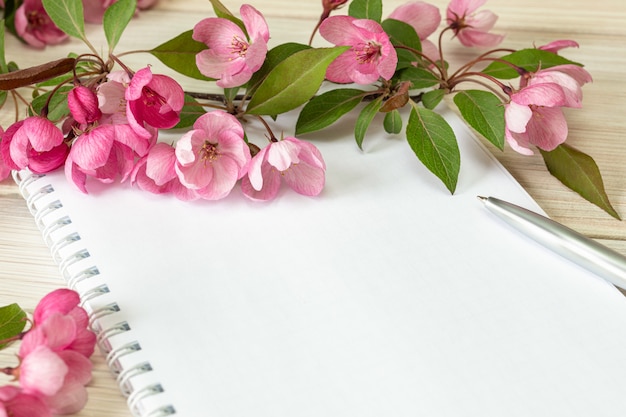 Una rama de un manzano floreciente y un cuaderno en blanco sobre una mesa de madera. Copia espacio