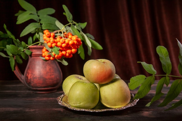 Rama de serbal con bayas y manzanas verdes sobre fondo de madera oscura y textil con espacio de copia