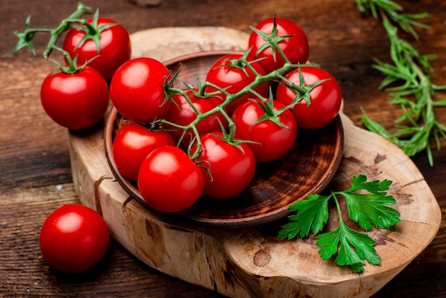 Rama de tomates cherry frescos con verduras sobre un fondo de madera marrón.
