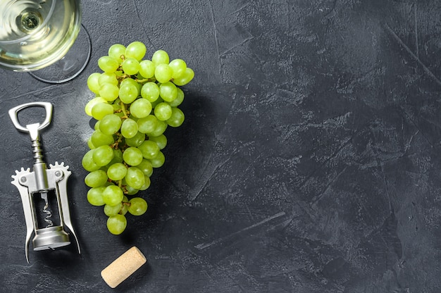 rama de uvas verdes, una copa de vino, un sacacorchos y un corcho. Concepto de vinificación. Fondo negro.